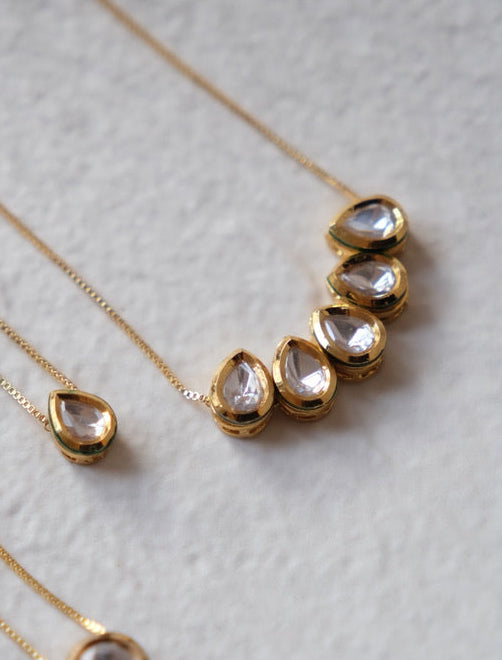 Gold necklaces with teardrop-shaped pendants on a light gray surface