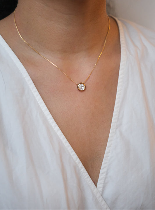 Gold necklace with a pendant on a person wearing a white top